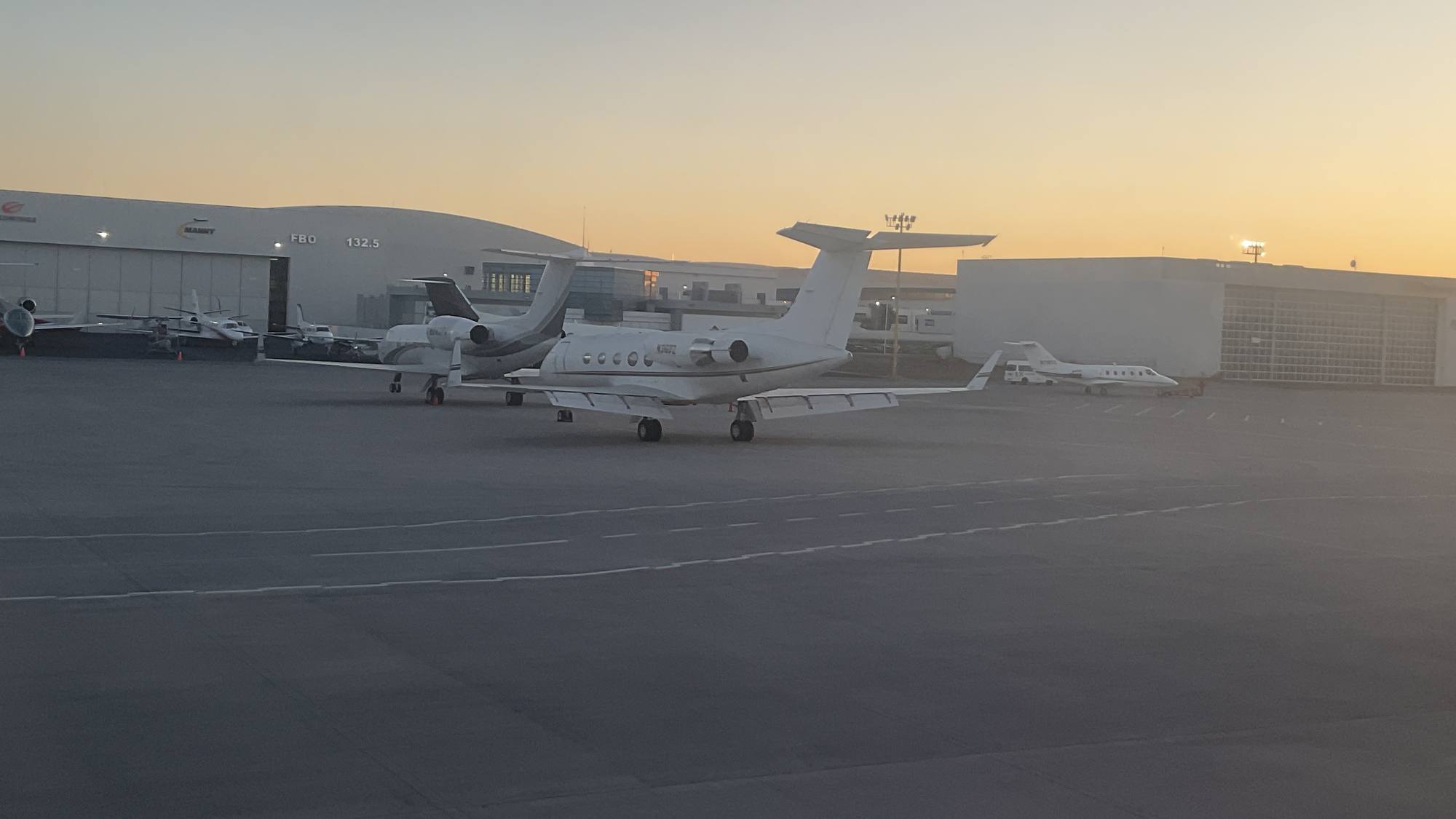 Business jets parked on an airport ramp at sunset